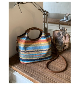 Détail du sac seau en paille arc-en-ciel avec poignées et bandoulière en similicuir brun