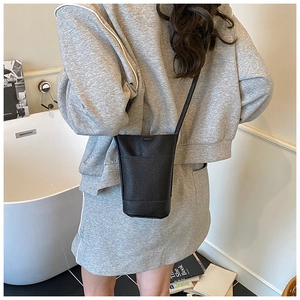 Detail of black lychee grain leather bucket crossbody bag worn in a modern studio