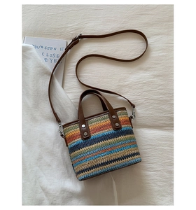 Gros plan du sac seau en paille colorée avec poignées en cuir marron et rivets argentés