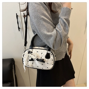 Detailed side view of cream pleated handbag with black bows and pearl strand charms