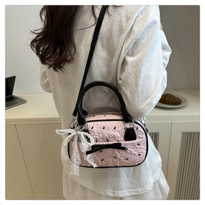 Detail view of pink embossed crossbody bag with black bows and pearl lace pendant charm