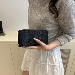 Handheld black snakeskin textured long wallet featuring a luxury gold zipper closure