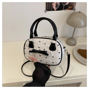Detail of mini bowling bag with black bow prints and silver hardware on a desk