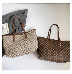Detail view of two large tote bags with monogram pattern and leather straps in workplace setting