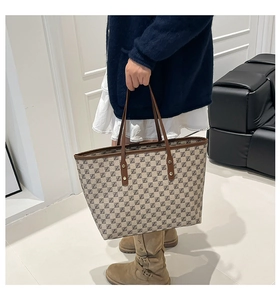 Detail of a large monogram tote bag with brown leather handles and golden metal rivets