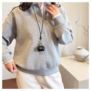 Detail of light grey textured sweatshirt paired with a black mini neck bag accessory