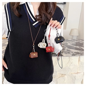 Miniature leather bag necklace charms in four colors worn by model in a modern room
