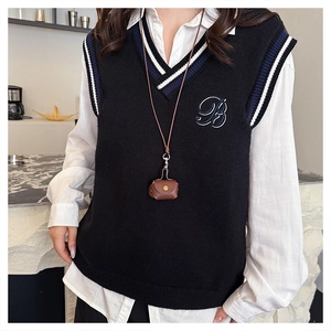 Detail of cute leather earphone pendant bag styled with a preppy knit vest and white shirt