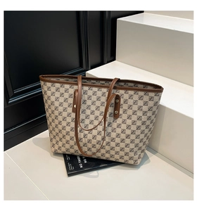 Detail of canvas tote bag with monogram print and brown leather handles on white stairs