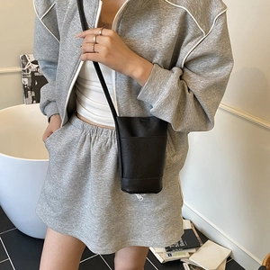 Mini black lychee leather crossbody bucket bag shown on a model in a minimalist setting