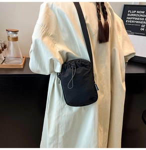 Détail d'un mini sac à bandoulière en nylon noir avec cordon de serrage et étiquette