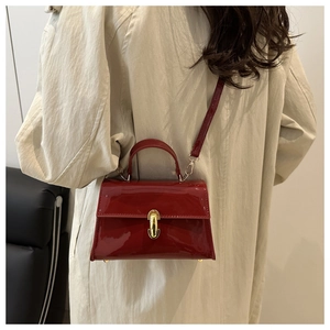 Detail of red patent leather crossbody bag with gold metal clasp on beige trench coat