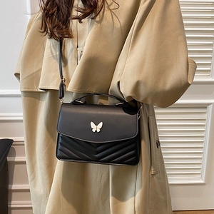 Chic black crossbody bag with V-quilting and white butterfly clasp on khaki coat