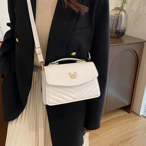 White leather flap bag with gold butterfly accent and V-quilted stitching on model