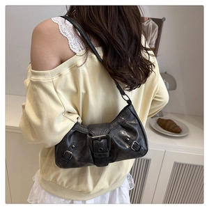 Detail of a vintage black shoulder bag with distressed leather and metal buckles on a model