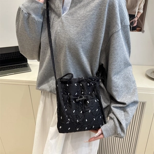 Quilted black crossbody bag with bow patterns and drawstring closure worn by model