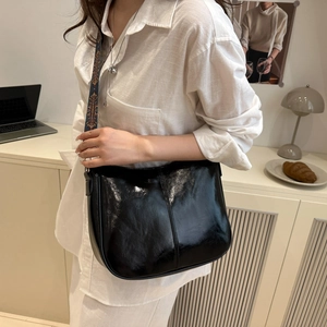 Minimalist black glossy shoulder bag with vintage ethnic embroidery strap worn by a model