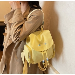 Detail of light yellow nylon backpack showing blue embroidered logo and drawstring closure