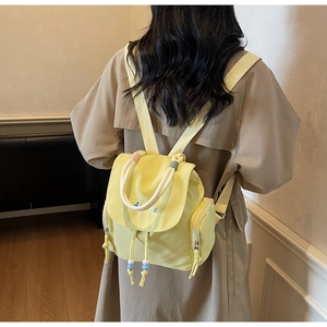 Detail of light yellow backpack with blue embroidery and colorful beaded drawstring