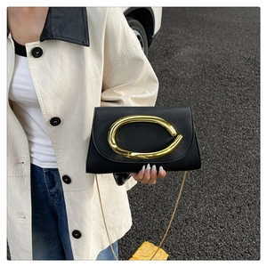 Détail de pochette en cuir noir avec grand anneau métallique doré et bandoulière chaîne