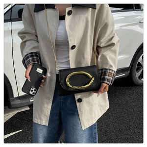 Détail de pochette en cuir noir avec grande boucle dorée et fine bandoulière chaîne