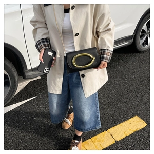 Détail d'une pochette en cuir noir avec boucle dorée ovale et bandoulière chaîne