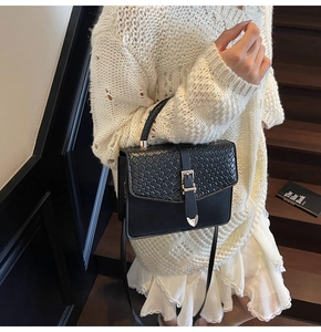 Detail of cross-woven pattern on black leather bag with gold buckle and adjustable strap