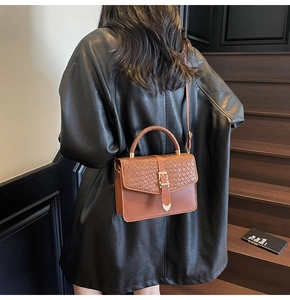 Détail du sac bandoulière marron avec rabat tressé et élégant accent métallique en cœur