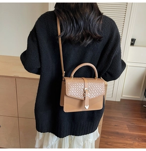 Model wearing a khaki brown crossbody bag with snake skin pattern flap and metal buckle
