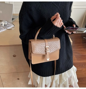 Detail of khaki crossbody bag featuring woven texture flap and golden heart buckle