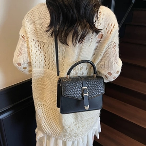 Chic black crossbody bag with woven texture and heart clasp worn by model on stairs