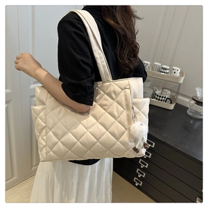 Detailed side view of off-white quilted tote bag with soft pom-pom charm on the shoulder