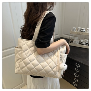Close-up of off-white quilted tote bag with side pocket and white plush pompom charm