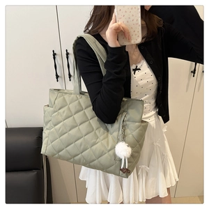 Close-up of light green quilted tote bag featuring a decorative white plush ball charm