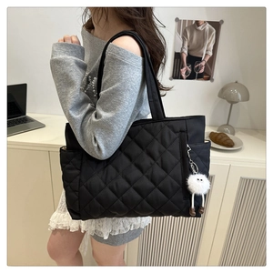 Close-up of black quilted tote bag featuring a cute plush monster charm in a cozy setting