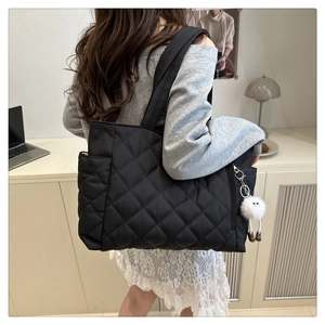 Macro view of black quilted puffer tote bag with monster plush charm for daily commute