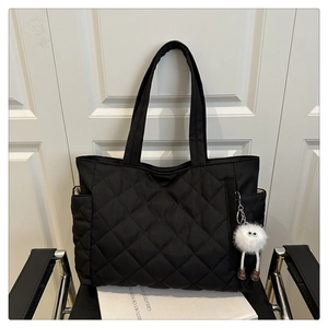 Detail of black quilted tote bag with side pocket and white plush eye charm accessory