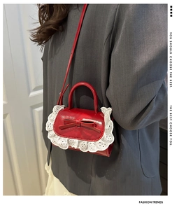 Detail of red leather crossbody bag featuring bow decoration and white lace trim