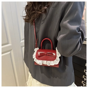 Detail of red bow mini bag with white lace trim and glossy patent leather finish