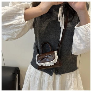 Close-up of small dark brown crossbody bag with white lace edges and bow detail