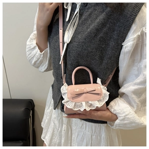 Detail view of pink bow handbag with white lace trim worn by model in gray vest