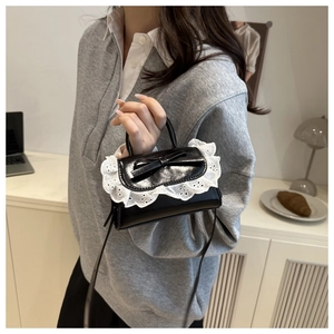 Miniature black glossy leather handbag featuring white lace embroidery and bow detailing