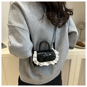 Detail of black mini crossbody bag with white lace trim and elegant bow decoration