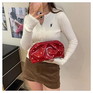 Détail de la pochette rouge en cuir verni avec des plis et des rivets dorés stylés
