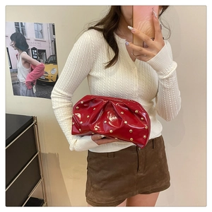 Détail de la pochette en cuir verni rouge avec texture plissée et rivets dorés brillants