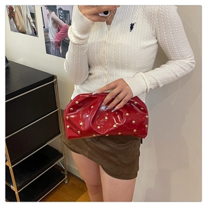 Détail d'une pochette en cuir verni rouge avec clous dorés et design plissé en nuage