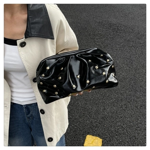 Détail de la pochette nuage en cuir verni noir avec rivets dorés et texture plissée