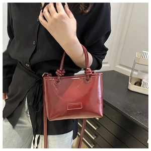 Detail of glossy dark red tote bag featuring unique knotted handles and smooth patent leather