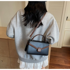 Detail of classic black and brown crossbody bag showing buckle and leather texture