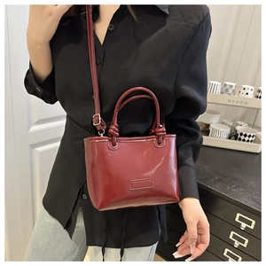 Detail of burgundy glossy patent leather tote bag with knotted handle and shoulder strap